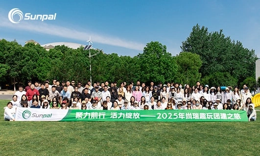 Gran equipo de Sunpal posando al aire libre en un día soleado sosteniendo una pancarta verde.